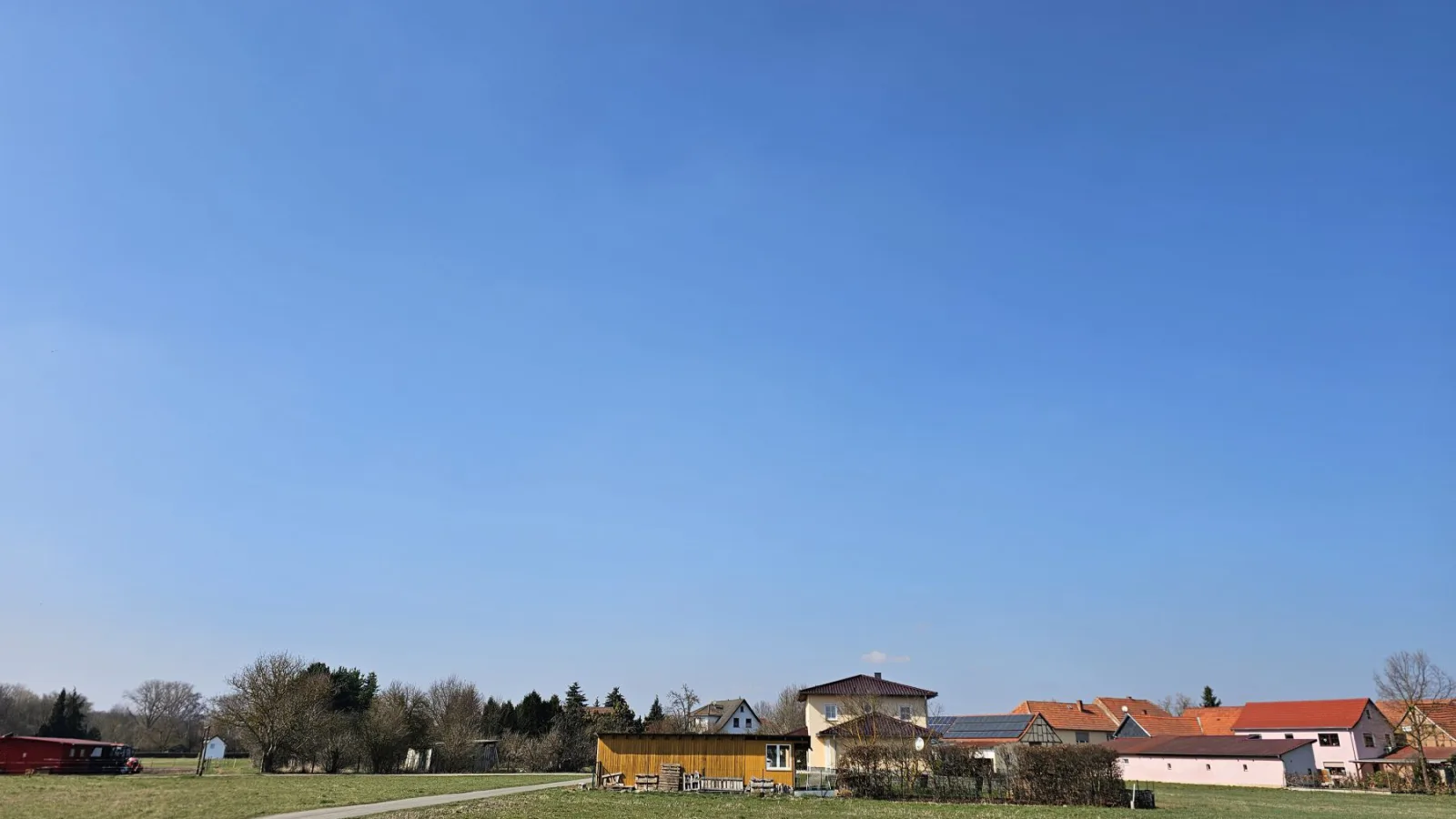 Weite Feldlandschaft mit Häusern am Ortsrand unter klarem blauem Himmel.